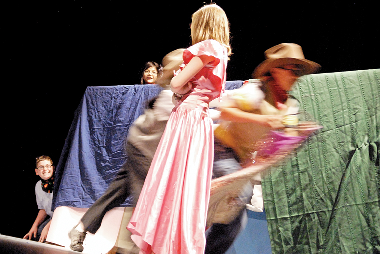 Seventh-grader Allie Dilldine stands still while actors run around her Tuesday on the Craig Middle School auditorium stage. Dilldine played Belinda in “Belinda and the Beast.” Peering from behind a stage set are seventh-graders Brandon Christensen and Angelica Bernal.