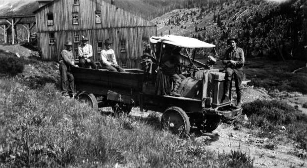 One b/w photograph of several men in a World War One army truck with solid rubber tires, 1920-. The photo was taken along Independence Pass, near the ghost town. The mill can be seen in the background.