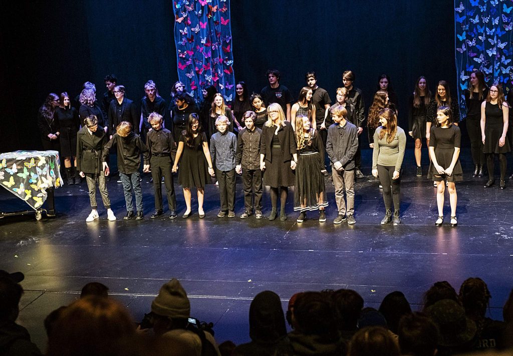 Aspen Middle School students and faculty stand on the stage holding hands and singing to John Lennon’s “Imagine” at the conclusion of the Holocaust Remembrance Day Ceremony in the Aspen District Theater on Thursday, Jan. 30, 2020. Decorated butterflies are displayed on stage to represent the children that passed through and died in the concentration camps. (Kelsey Brunner/The Aspen Times)