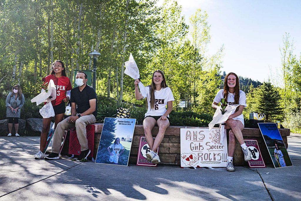 Aspen’s girls soccer seniors Karen Galvan, left, Payton Curly and Maeve McGuire watch with their families as their team has a mini drive-by parade with signs and honking to honor them during a rose ceremony in the Aspen Recreation Center parking lot on Monday, May 18, 2020. (Kelsey Brunner/The Aspen Times)