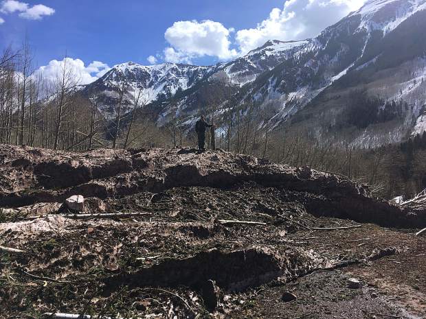 A man stands on the top of avalanche debris covering Maroon Creek Road in mid-April.