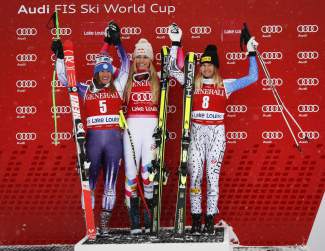Lindsey Vonn, center, of the United States, celebrates her first place finish on the podium with teammate and second-place finisher Stacey Cook, left, and third-place finisher and teammate Julia Mancuso following the women's World Cup downhill ski race in Lake Louise, Alberta, Saturday, Dec. 6, 2014. (AP Photo/The Canadian Press, Jeff McIntosh)