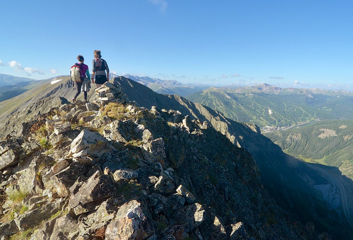 Local hikers Sara Skinner (purple) and Ben Trollinger survey the approach to Peak Four (12,866 feet) from the summit of Peak Three (12,676 feet). The 0.75-mile stretch between the two peaks is deceptively difficult, featuring either a razor-thin ridgeline traverse or a descent on a west-facing boulder field before an ascent to the summit.
