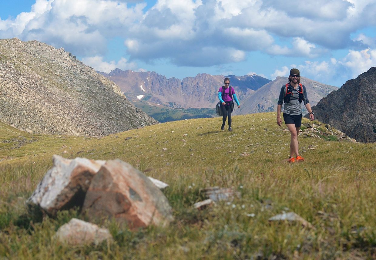 Local hikers Sara Skinner (purple) and Ben Trollinger hike on relatively smooth and forgiving terrain between Peak Four (12,866 feet) and Peak Five (12,855 feet) during an attempt of the Tenmile Traverse. The sheer, reddish face of the Gore Range is in the background.
