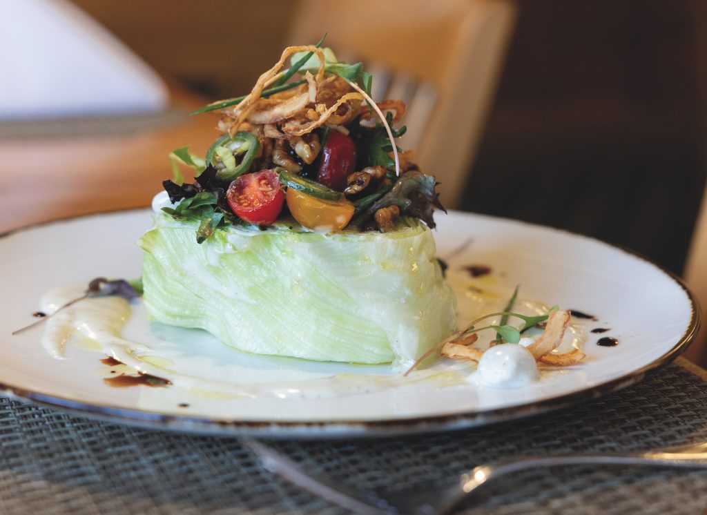 Wedge salad with cherry tomatoes, bacon lardons, fresh chives, candied walnuts, blue cheese dressing and crispy onions.