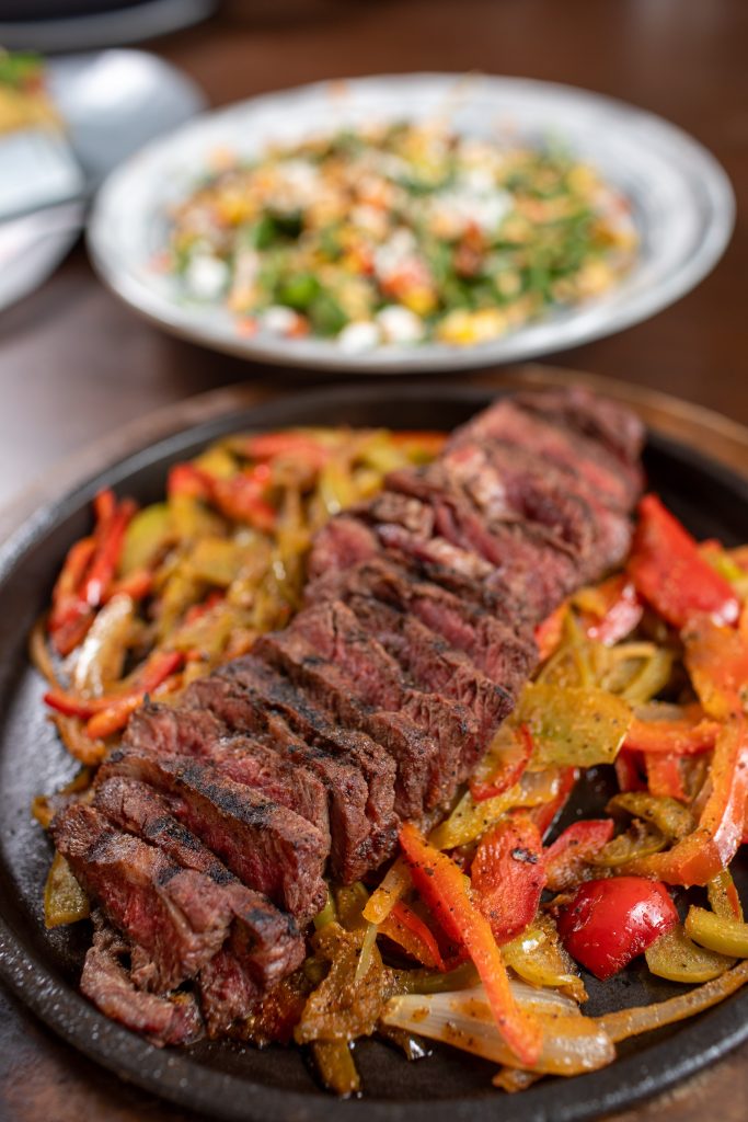 Flame-grilled fajitas with chili-rubbed flatiron steak, sweet peppers and onions, warm tortillas, black beans, cilantro-lime rice and all the fixings.