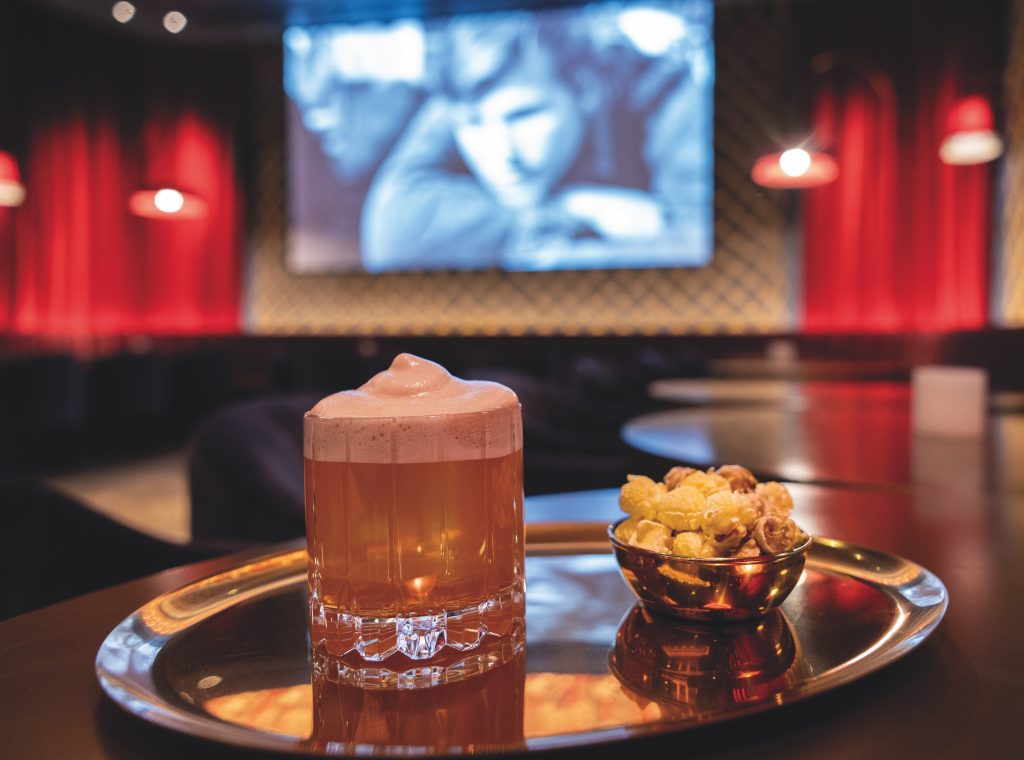 The Last Picture Show cocktail with Balcones Texas rye, popcorn syrup, and Dr. Pepper foam, served with cheddar-caramel popcorn.
